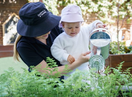 Explore & Develop Educator and child watering the garden
