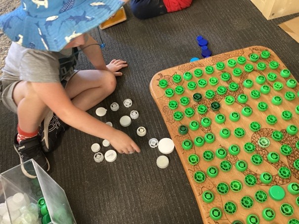 Preschool child sorting recycled bottle tops. 